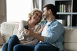© fizkes - Smiling young man showing funny online video or vacation photos on smartphone to laughing middle aged 60s mother, relaxing together on sofa at home, overjoyed family entertaining with tech device.