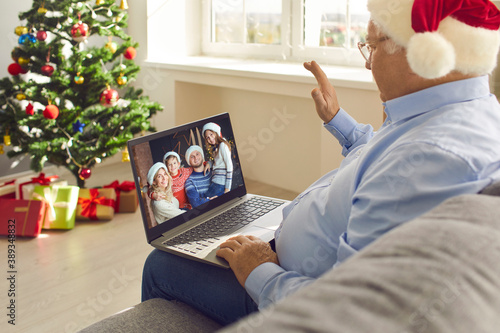 Grandpa video calling family on Christmas Day and waving hand at screen happy to see grandchildren