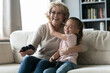 © fizkes - Happy little preschool adorable child girl embracing joyful excited elderly senior retired grandmother, celebrating video game competition win in living room, family domestic activity concept.