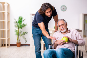 Old man in wheel-chair and young bad caregiver indoors