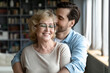 © fizkes - Happy middle aged older woman in eyeglasses standing with closed eyes, enjoying tender loving moment with grown son at home. Devoted young man showing care to smiling retired old mother indoors.