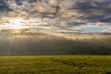 Fototapeta  - sunrise in misty mountain valley with green fields and fall color forest