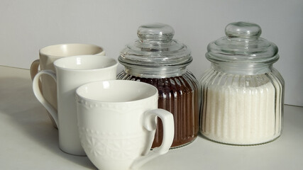      two glass bottles with coffee and sugar. three empty white cups on the table                                                                                        