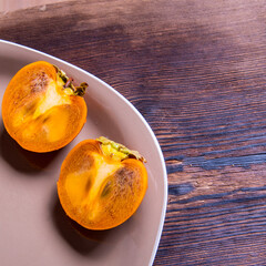 Persimmon cut in half on a plate on a wooden table, close-up, copy space