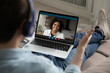 © fizkes - Rear view man wearing headphones chatting with smiling woman online, sitting on couch, using laptop, boyfriend talking with diverse girlfriend, using webcam and social media app, making video call