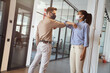 © Kostiantyn - Two young diverse colleagues wearing face protective masks bumping elbows, greeting each other while standing in the modern office