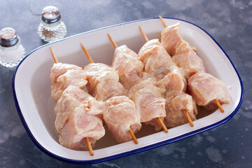 Wall Mural - Step by step cooking chicken skewers on wooden skewers from chicken breast fillet, step 4 - stringing marinated chicken fillet on wooden skewers and laying it on a dish before baking, horizontal