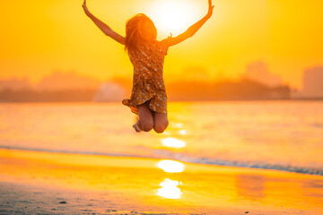 Wall Mural - Adorable happy little girl on white beach at sunset.