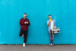 © Davide Zanin - Cool men looking at mobile phone lean against blue wall - Couple of influencer guys listening music with vintage boombox stereo outdoor in the street - Concept of tech, social network and music trends