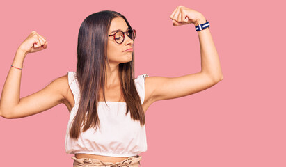 Young hispanic woman wearing casual clothes and glasses showing arms muscles smiling proud. fitness concept.