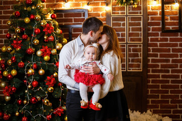 A happy family with a small child stands near a Christmas tree with toys and gifts. Happy childhood. New Year's festive atmosphere. Family relationship concept