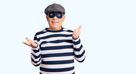 Canvas Print - Senior handsome man wearing burglar mask and t-shirt showing palm hand and doing ok gesture with thumbs up, smiling happy and cheerful