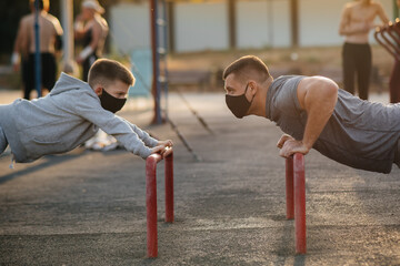 Father and son play sports on the sports field in masks during sunset. Healthy parenting and healthy lifestyle