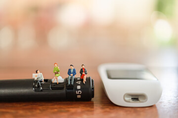 Group of Businessman and woman miniature figure sitting on lancet with glucose meter on wooden table using as diabetes, glycemia, health care and people concept.