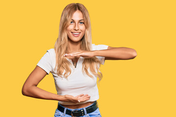 Sticker - Beautiful blonde young woman wearing casual white tshirt gesturing with hands showing big and large size sign, measure symbol. smiling looking at the camera. measuring concept.