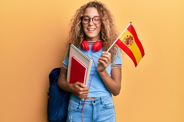 Poster - Beautiful caucasian teenager girl exchange student holding spanish flag winking looking at the camera with sexy expression, cheerful and happy face.