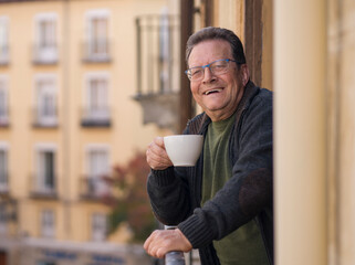 lifestyle portrait of happy and cheerful mature man 65 to 70 years old at home balcony feeling positive and relaxed drinking coffee enjoying retirement smiling to the street view