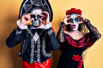 Canvas Print - Young couple wearing mexican day of the dead costume over yellow trying to open eyes with fingers, sleepy and tired for morning fatigue