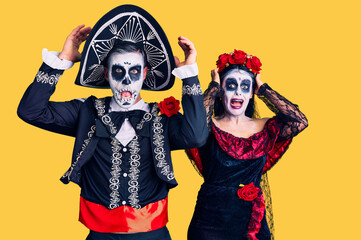 Canvas Print - Young couple wearing mexican day of the dead costume over background crazy and scared with hands on head, afraid and surprised of shock with open mouth