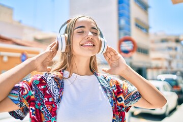 Young beautiful blonde caucasian woman smiling happy outdoors on a sunny day wearing headphones listening to music