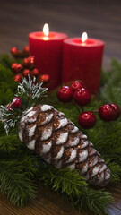 Red candles with fir branches and a toy pine cone. Dark Christmas and New Year background. Red candles, green spruce branches, red berries.