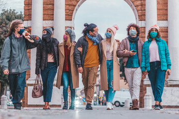 Wall Mural - young friends walking on city street - new normal lifestyle concept with group of people with face m