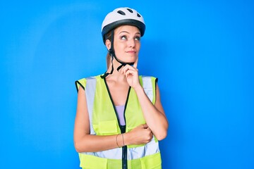 Wall Mural - Young caucasian girl wearing bike helmet and reflective vest serious face thinking about question with hand on chin, thoughtful about confusing idea