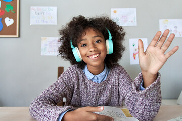 Happy african american kid child girl wearing headphones waving hand talking with remote teacher on social distance learning video conference call chat class, headshot zoom portrait, web cam view.