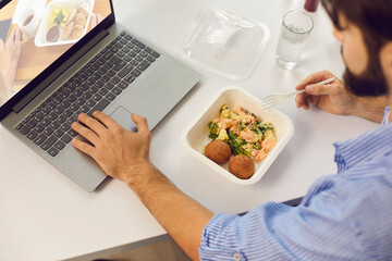 Man having lunch in the office, eating takeaway meal and visiting food delivery website