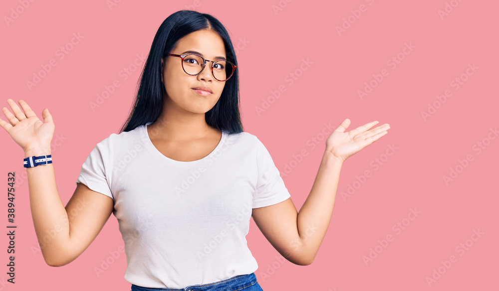 Young beautiful asian girl wearing casual clothes and glasses clueless and confused expression with arms and hands raised. doubt concept.