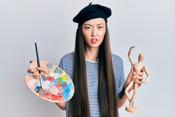 Sticker - Young chinese woman wearing artist look with beret holding manikin clueless and confused expression. doubt concept.