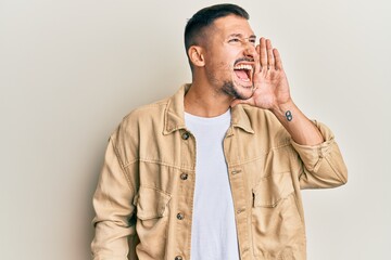 Wall Mural - Handsome man with tattoos wearing casual brown denim jacket shouting and screaming loud to side with hand on mouth. communication concept.