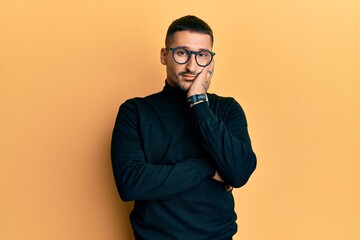 Canvas Print - Handsome man with tattoos wearing turtleneck sweater and glasses thinking looking tired and bored with depression problems with crossed arms.