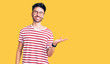 © Krakenimages.com - Young hispanic man wearing casual clothes smiling cheerful presenting and pointing with palm of hand looking at the camera.