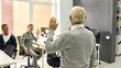 © Svitlana - Back view of aged man, senior intern waving, greeting young colleagues at his new job in the modern office