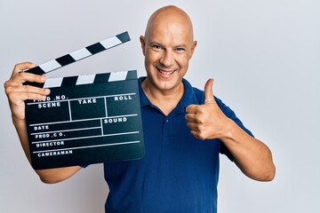 Wall Mural - Middle age bald man holding video film clapboard smiling happy and positive, thumb up doing excellent and approval sign