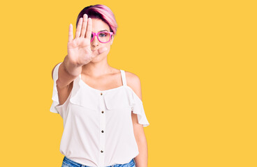 Canvas Print - Young beautiful woman with pink hair wearing casual clothes and glasses doing stop sing with palm of the hand. warning expression with negative and serious gesture on the face.