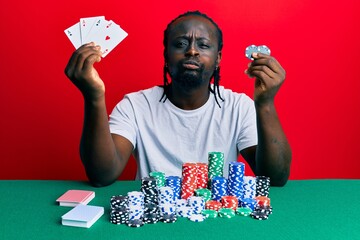 Sticker - Handsome young black man sitting on the table with poker chips and cards puffing cheeks with funny face. mouth inflated with air, catching air.