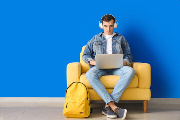 Canvas Print - Male student with laptop studying online near color wall