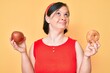 Brunette woman with down syndrome holding red apple and donut sitting smiling looking to the side and staring away thinking.