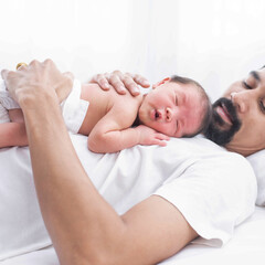 Poster - father with a baby girl at home sleeping. side view of a young man playing with his little baby in bed. a portrait of a young Asian father holding his adorable baby on white background.