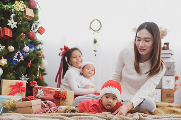 Wall Mural - parent and three little children having fun and playing together near christmas tree indoors. merry christmas and happy holidays. cheerful mom and her cute daughters girls exchanging gifts.