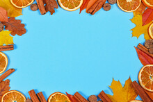 Colorful Autum Leaves, Cinnamon Sticks And Dried Orange Slices Forming Border Around Blue Background With Empty Copy Space