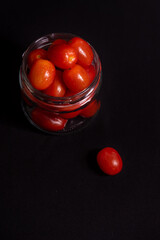 low key photo of cherry tomatoes in a glass jar isolated on black background