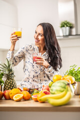 Wall Mural - Good-looking brunette looks at a glass of yellow juice in one hand, holding red juice in the other hand