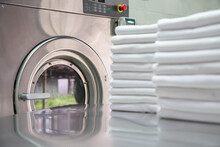 Stack Of Clean Bed Sheets In Front Of Industrial Washing Machine. Focused On Washing Machines. 
Shot Taken In The Factory.