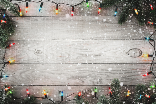 Cuadros en Lienzo Christmas background - Christmas lights bulb and fir branch and snowflake on rustic wood table, frame border design