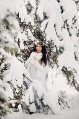 Portrait of a woman in white clothes in a cold winter forest. Girl with a wreath on her head in a snow-covered winter forest