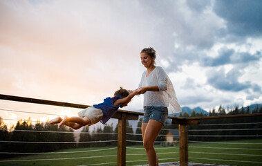 Wall Mural - Mother with small daughter playing on patio of wooden cabin, holiday in nature concept.