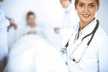 Wall Mural - Female doctor smiling on the background with patient in the bed and two doctors